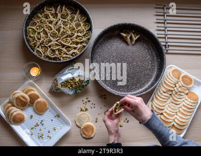 Hände halten Qatayef gefüllt mit Schokolade und mit Pistazien belegt auf einem Holztisch, mit einem Teller, der später im Ofen als Ramadan swe zubereitet wird Stockfoto