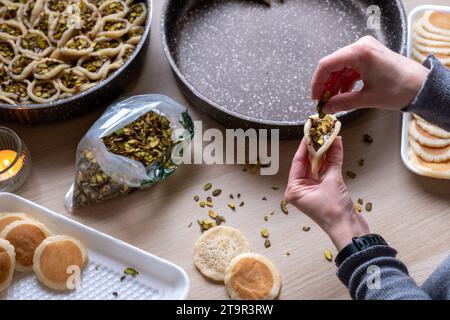 Hände halten Qatayef gefüllt mit Schokolade und mit Pistazien belegt auf einem Holztisch, mit einem Teller, der später im Ofen als Ramadan swe zubereitet wird Stockfoto