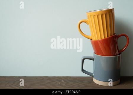 Stapel bunte Keramikbecher auf Holztisch. Blauer Wandhintergrund Stockfoto