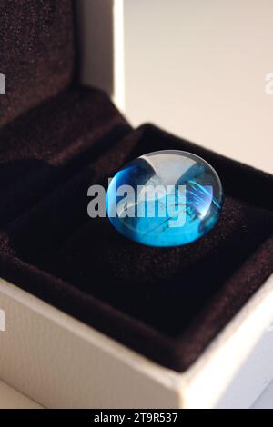 Glatter blauer Glasstein auf einem schwarzen Samtkissen in einer eleganten Geschenkbox detailliertes Stockfoto Stockfoto