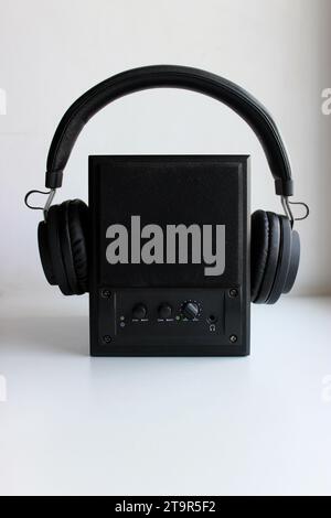 Schwarze Kopfhörer an einem schwarzen Audiolautsprecher, Vorderansicht Stockfoto