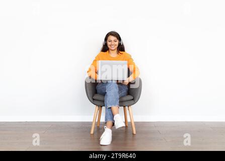 Fröhliche junge indianerin, die Laptop und Kopfhörer benutzt Stockfoto