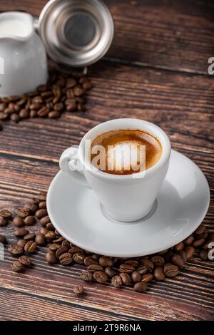 Espresso Macchiato in weißer Porzellanschale mit Milch und Kaffeebohnen auf Holztisch Stockfoto