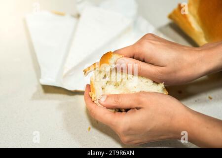 Blick von oben auf frisches Brotbrot, das von weiblichen Händen geöffnet wird, mit einem Stück Brie-Käse im Hintergrund Stockfoto