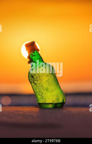 Flasche am Strand, Sand und Wasser während des goldenen Sonnenaufgangs über dem Horizont Stockfoto