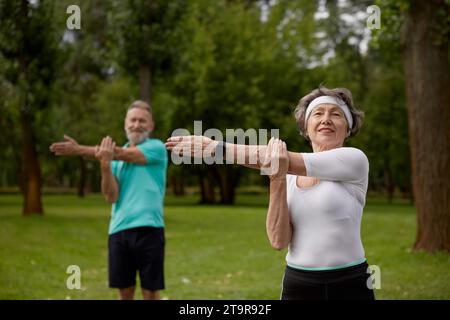 Seniorenpaar, das während des Physiotherapiekurses auf der Natur Aufwärmübungen macht Stockfoto