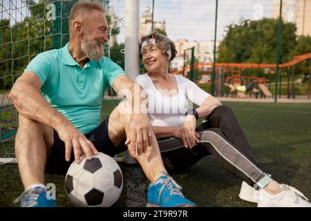 Glückliches lächelndes und müdes Seniorenpaar, das sich nach erfolgreichem Fußballtraining erholt Stockfoto