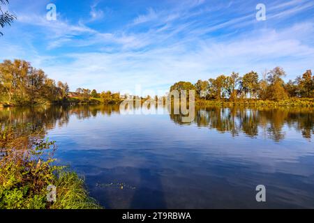 Landschaft eines Flusses umgeben von Herbstbäumen vor blauem Himmel im Hintergrund, Spiegelreflexion auf der Wasseroberfläche, belgisches Naturschutzgebiet de Wissen M Stockfoto