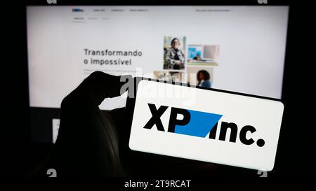 Person mit Smartphone und Logo der brasilianischen Investmentverwaltungsgesellschaft XP Inc. Vor der Website. Schwerpunkt auf dem Display des Telefons. Stockfoto
