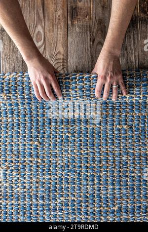 Mann, der Hand gewebte geometrische Denim-Teppich auf einem Holzboden zu Hause rollte. Stockfoto
