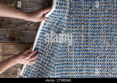 Mann, der Hand gewebte geometrische Denim-Teppich auf einem Holzboden zu Hause rollte. Stockfoto