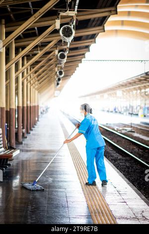 Eine thailändische Reinigungsfrau macht sich auf dem Bahnsteig auf und wischt Schmutz und Staub im Bahnhof Hua Lamphong, Bangkok, Thailand. Stockfoto