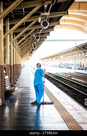 Eine thailändische Reinigungsfrau macht sich auf dem Bahnsteig auf und wischt Schmutz und Staub im Bahnhof Hua Lamphong, Bangkok, Thailand. Stockfoto