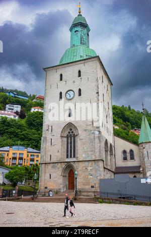 Bergen, Norwegen, 22. Juni 2023: Die Kathedrale von Bergen, hier mit bewölktem Himmel und Menschen, die durch die kopfsteingepflasterten Straßen laufen, ist der Bischofssitz von Bergen Stockfoto