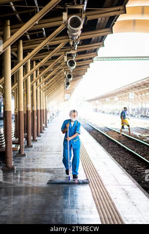 Eine thailändische Reinigungsfrau macht sich auf dem Bahnsteig auf und wischt Schmutz und Staub im Bahnhof Hua Lamphong, Bangkok, Thailand. Stockfoto