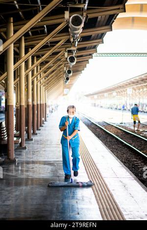 Eine thailändische Reinigungsfrau macht sich auf dem Bahnsteig auf und wischt Schmutz und Staub im Bahnhof Hua Lamphong, Bangkok, Thailand. Stockfoto