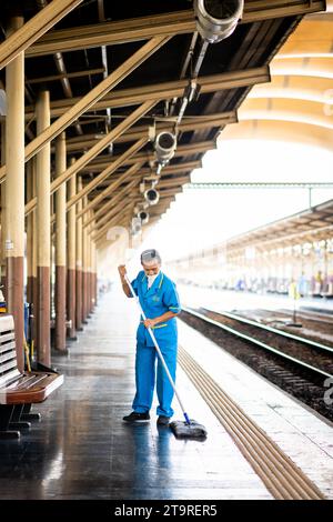 Eine thailändische Reinigungsfrau macht sich auf dem Bahnsteig auf und wischt Schmutz und Staub im Bahnhof Hua Lamphong, Bangkok, Thailand. Stockfoto