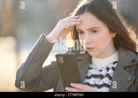 Besorgte Frau, die schlechte Nachrichten am Telefon auf der Straße überprüft Stockfoto