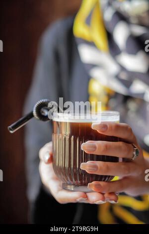 Nahaufnahme einer Frau, die eine Tasse Eiskaffee mit einem Strohhalm hält. Stockfoto