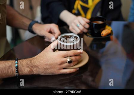 Nahaufnahme von männlichen Händen, die eine Tasse Kaffee am Tisch halten, und einer weiblichen Hand, die eine Tasse Kaffee im Hintergrund hält. Stockfoto