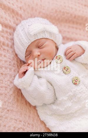 Neugeborenes Mädchen im weißen Strick-Outfit auf rosa Decke Stockfoto