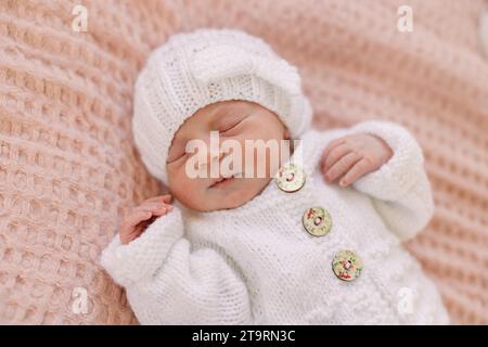 Neugeborenes Mädchen im weißen Strick-Outfit auf rosa Decke Stockfoto