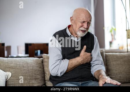 Ein älterer Mann leidet an Brustschmerzen, während er zu Hause auf dem Sofa sitzt Stockfoto