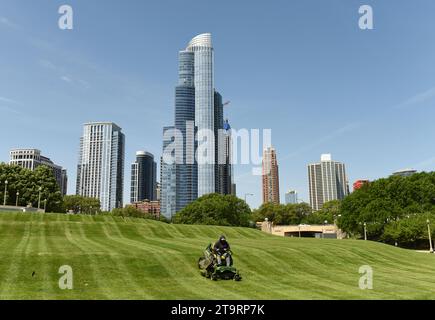 Chicago, USA - 5. Juni 2018: Arbeiter, die Gras im Great Ivy Lawn im Field Museum Park mähen, mit Chicagoer Wolkenkratzern im Hinterland. Stockfoto