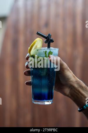 Mann hält ein Glas kaltes Getränk, ein Stück Zitrone wird oben auf das Glas gelegt, Schwarzes Trinkhalm Stockfoto