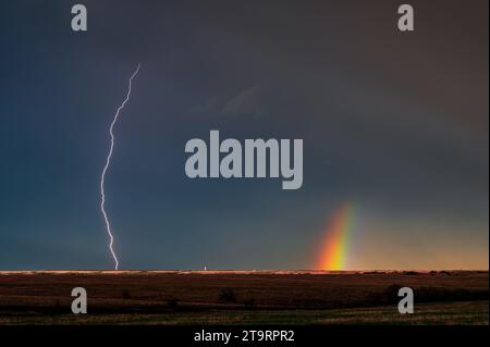 Ein Regenbogen und ein brillanter Blitz Streifen über den Himmel über dem Feld Stockfoto