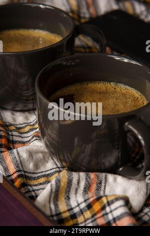 Zwei schwarze Tassen Kaffee auf einem karierten Tuch, umgeben von einem Buch und Zucker Stockfoto