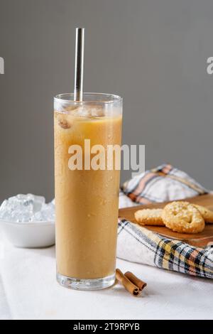 Ein Eiskaffee serviert mit einem Stahlkaffee in einem Trinkglas, auf einer weißen Tischdecke mit Zimt und einer Schüssel voller Eis. Zwei Kekse sitzen darauf Stockfoto