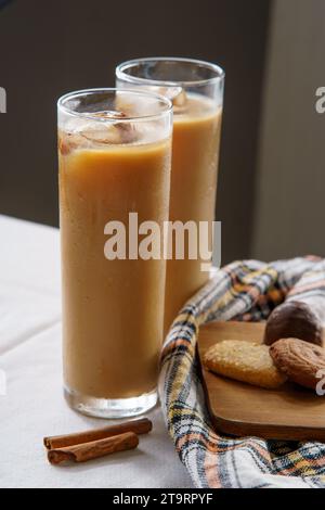 Zwei Eiskaffees in einem Trinkglas auf einer weißen Tischdecke mit Zimt. Zwei Kekse sitzen auf einem Holzbrett mit einem karierten Tuch. Stockfoto