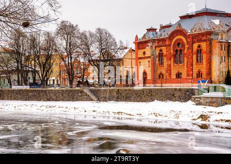 uschgorod, ukraine - 9. JAN 2017: Stadtbild mit gefrorenem Fluss und rotem Gebäude einer Synagoge auf dem Damm. Winterferien, weihnachtsfest im Stockfoto