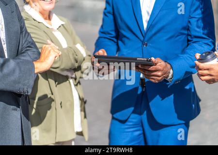 Nahaufnahme der Hände eines Geschäftsmannes, der im Freien ein digitales Tablet nutzt und von anderen Geschäftsleuten umgeben ist Stockfoto