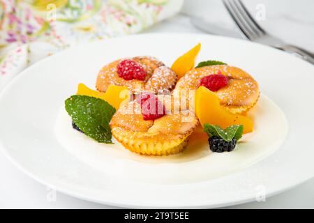 Muffins mit Pfirsich, Himbeere, schwarzer Beere und Minze mit Puderzucker, Seitenansicht Stockfoto