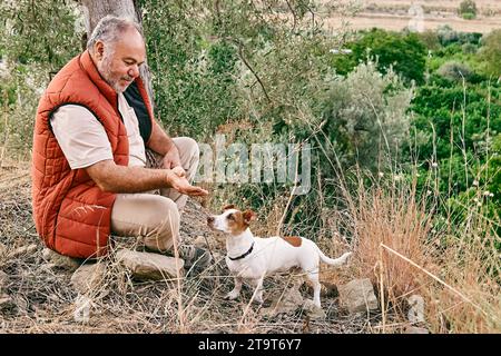 Reifer grauhaariger Mann, der Zeit im Freien mit seinem kleinen süßen Jack Russell Terrier in der Bergwelt verbringt. Stockfoto