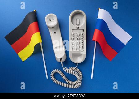 Altes Telefon und zwei Flaggen auf blauem Hintergrund, Konzept zum Thema Telefongespräche zwischen Deutschland und Russland Stockfoto
