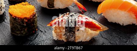 Unagi-Sushi, Nigiri mit Aal und anderes Sushi und Brötchen auf schwarzem Hintergrund. Ein Panorama Stockfoto
