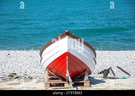 Ein rotes Boot, das an der Küste steht, mit blauem Meer im Hintergrund in Etretat Stockfoto