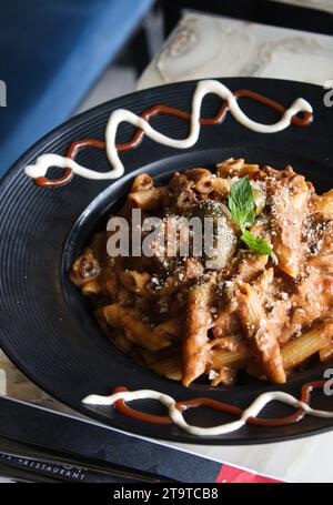 Penne Pasta mit Sauce, Oliven und frisch geriebenem Parmesankäse, auf einer schwarzen Platte, mit Sauce an der Seite. Stockfoto