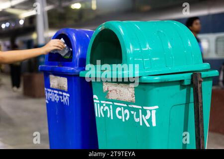 Dhanbad, Jharkhand, Indien - 26. Oktober 2023: Grüne und blaue Mülltonne auf dem Bahnsteig der indischen Eisenbahn, die von einer Hand eines Kindes benutzt wird Stockfoto