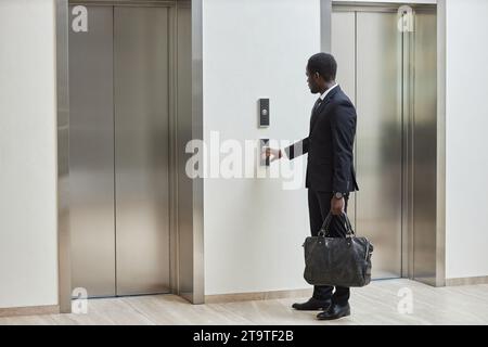 Vollständige Aufnahme eines afroamerikanischen Geschäftsmannes in elegantem Anzug, der den Knopf drückt, während er die Ledertasche im Business Center hält, Kopierraum Stockfoto