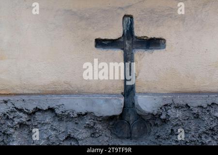 Ein Holzkreuz ist in einen ausgehöhlten Abschnitt einer Stuck- und Zementwand eines Gebäudes eingebettet. Stockfoto