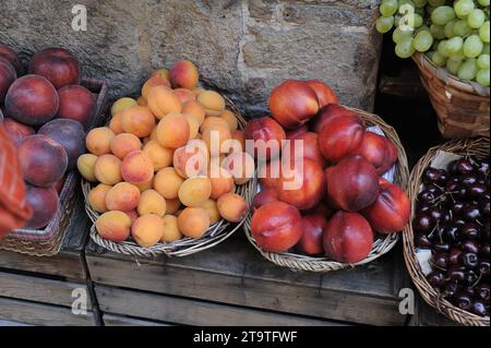 Körbe mit frischen Pfirsichen, Pflaumen, Aprikosen, Kirschen, Trauben und Nektarinen auf Holzkisten auf einem Erzeugnismarkt in Italien. Stockfoto