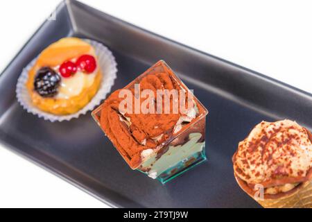 Blick von oben auf den köstlichen Tiramisu-Kuchen in der Nähe von kleinen Kuchen auf schwarzem Gericht Stockfoto