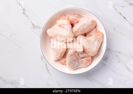 Rohe Hähnchenflügel in weißer Schüssel, zum Kochen auf Marmorhintergrund vorbereitet Stockfoto