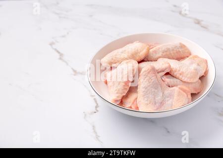 Rohe Hähnchenflügel in weißer Schüssel, zum Kochen auf Marmorhintergrund vorbereitet Stockfoto