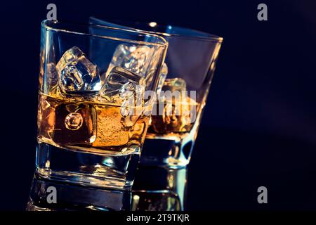 Zwei Gläser Whiskey mit Eiswürfeln auf schwarzem Hintergrund mit hellblauem Hintergrund und Reflexion, Zeit der Entspannung mit Whisky Stockfoto