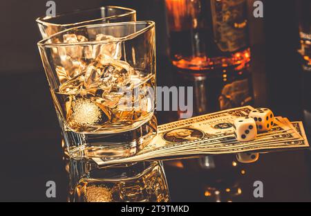 Gläser Whiskey in der Nähe der Flasche auf Dollar Geld und Spielwürfel auf einem schwarzen Tisch. Alter westlicher Stil, kalte Atmosphäre Stockfoto